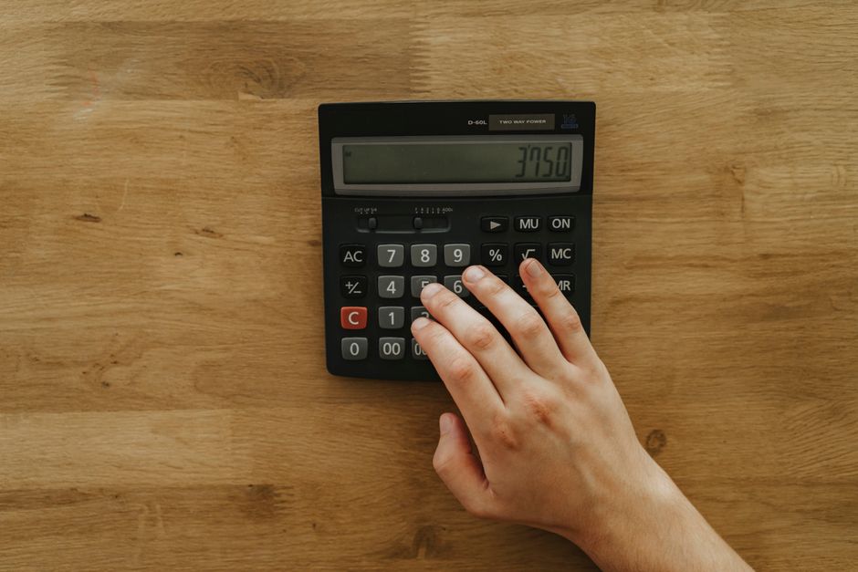 2026년 6월 19일 한국 금융시장 동향 — A person's hand pressing keys on a calculator displaying 3750 on a wooden table, top view.