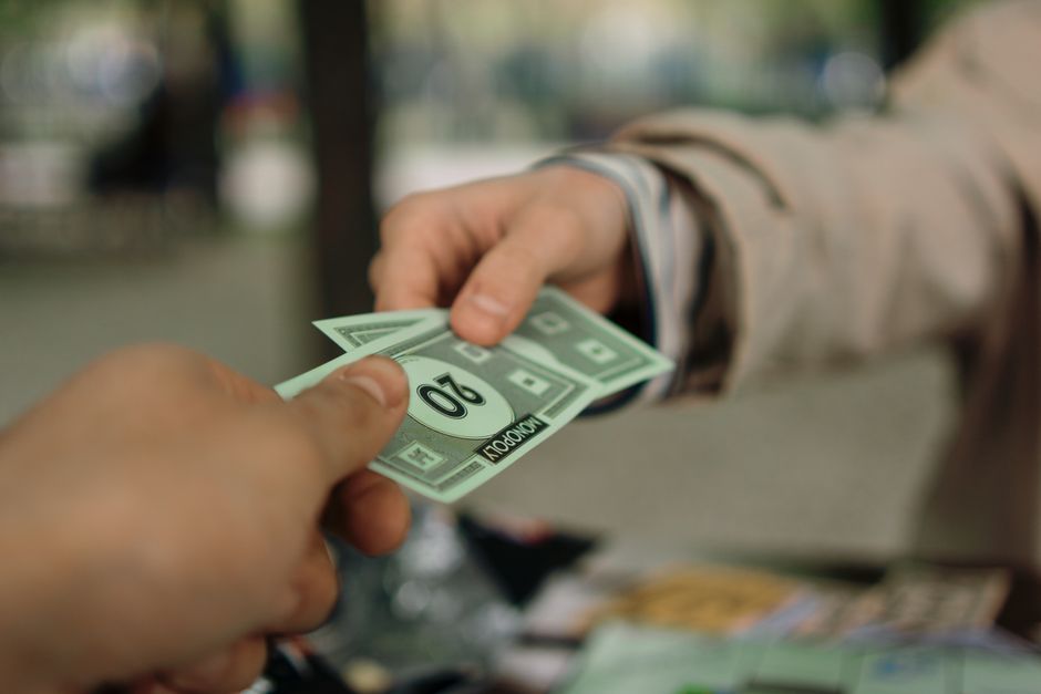 한국 금융시장 동향 — 2026년 8월 28일(금) — Close-up of hands exchanging Monopoly money outdoors in a park setting.